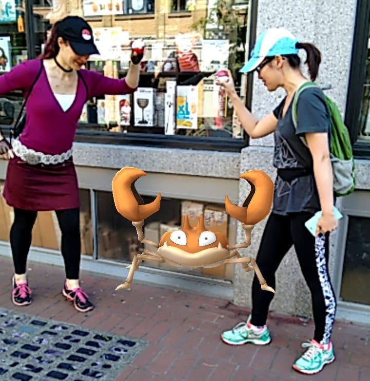 Two females holding Pokeballs playing PokemonGO, a kids entertainment game, on the sidewalk