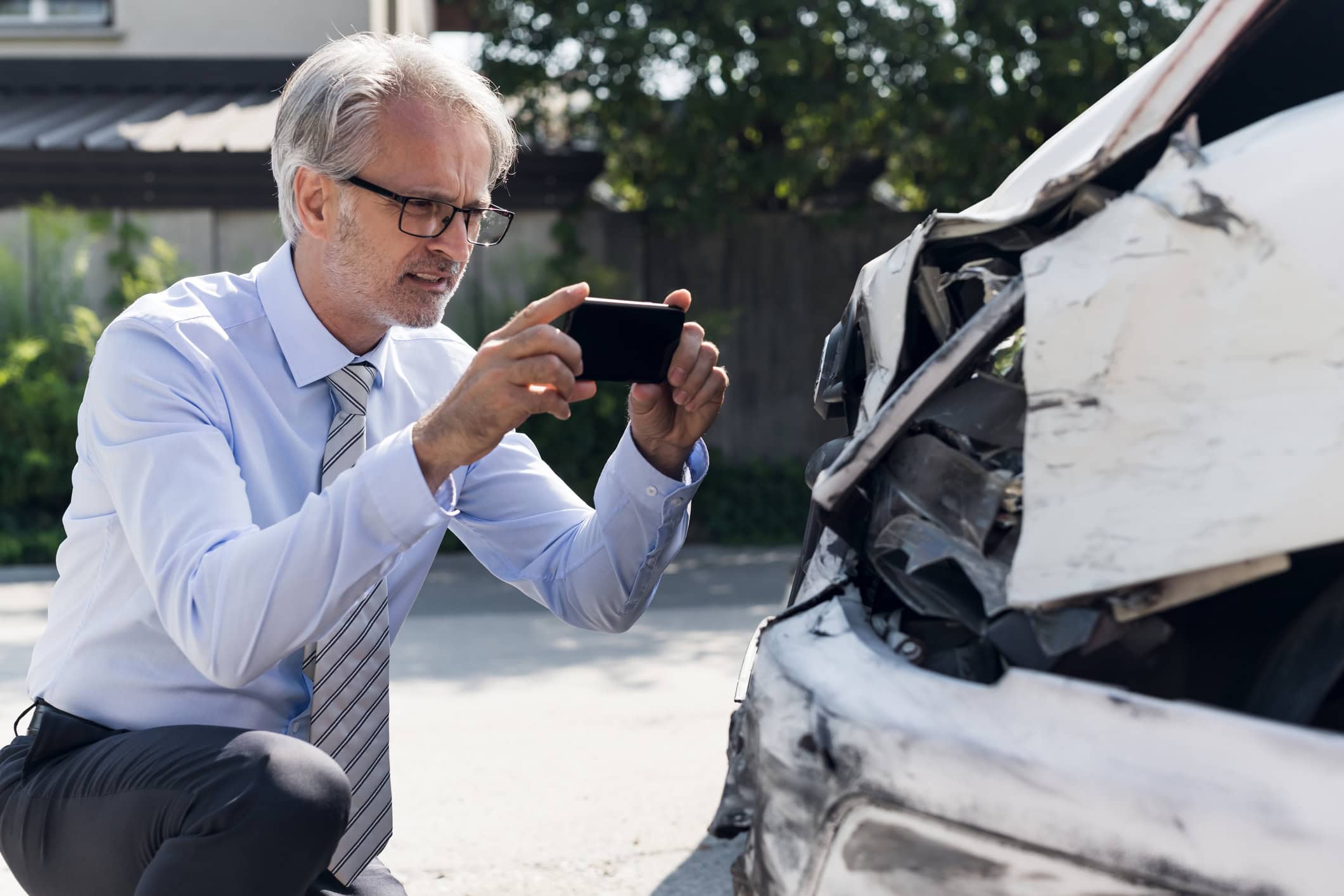 Photo of a man holding his cell phone up to take a picture of car accident damage