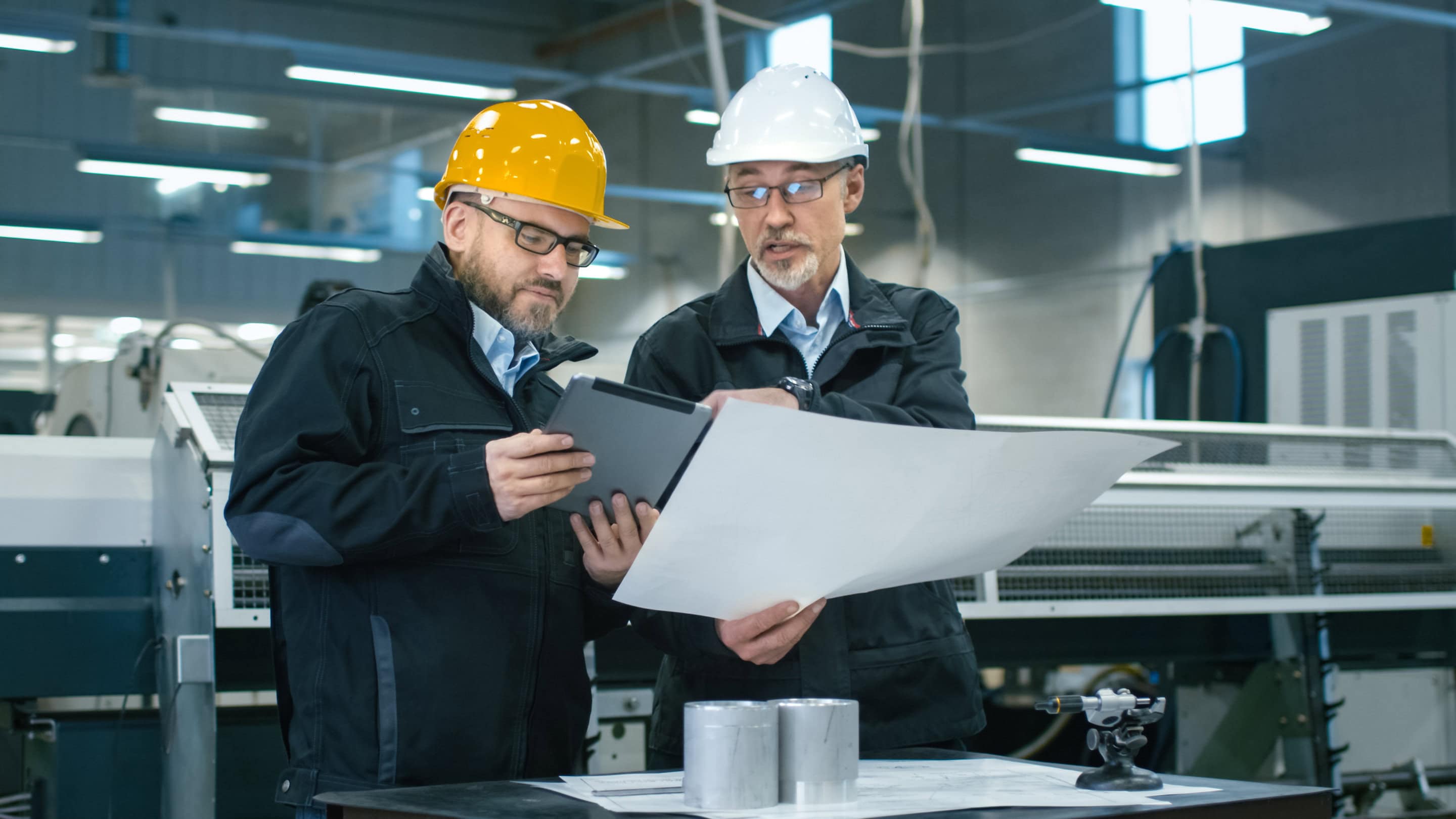 Two engineers discuss a blueprint while checking information on a mobile device.
