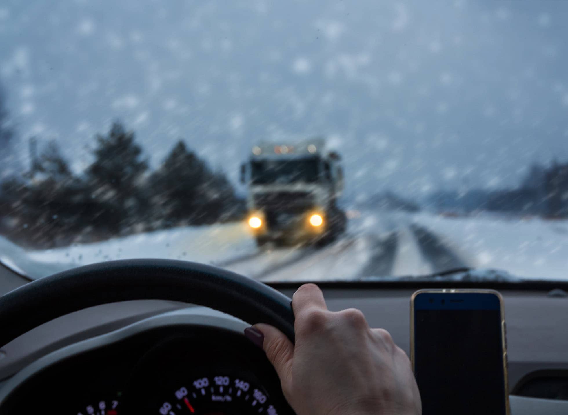 View from inside a car driving on a snowy highway with an oncoming truck ahead